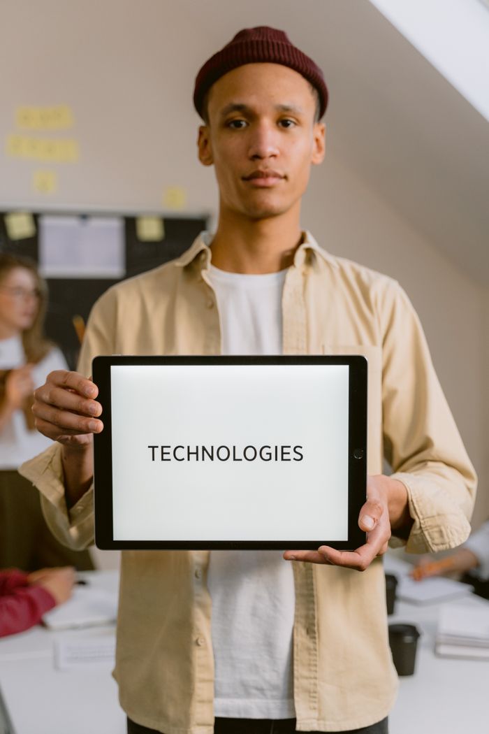 services-03 A young man holding a tablet displaying the word 'Technologies' in an indoor office setting.